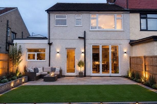 Design visualisation of the same house with a flat-roof side extension, bi-fold doors and a landscaped patio